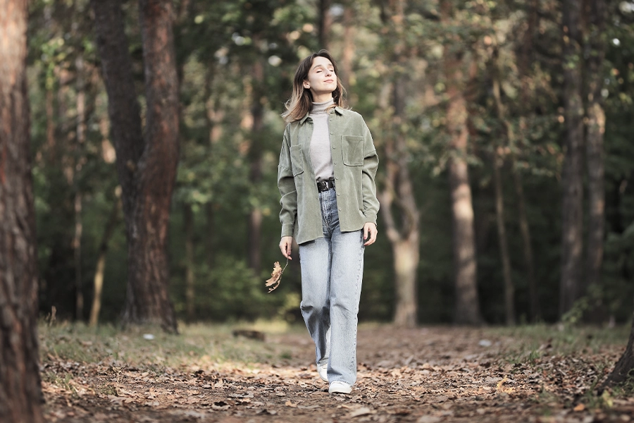 Mädchen mit grünem Shirt und blauen Jeans im herbstlichen Wald, das ein Ahornblatt in den Händen hält