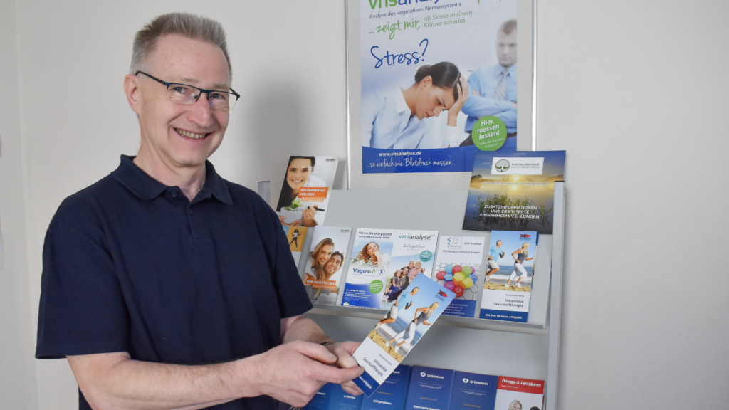 Dr. Pape posiert lächelnd und zeigt einen Flyer, der erklärt, wie man Stress reduzieren kann.